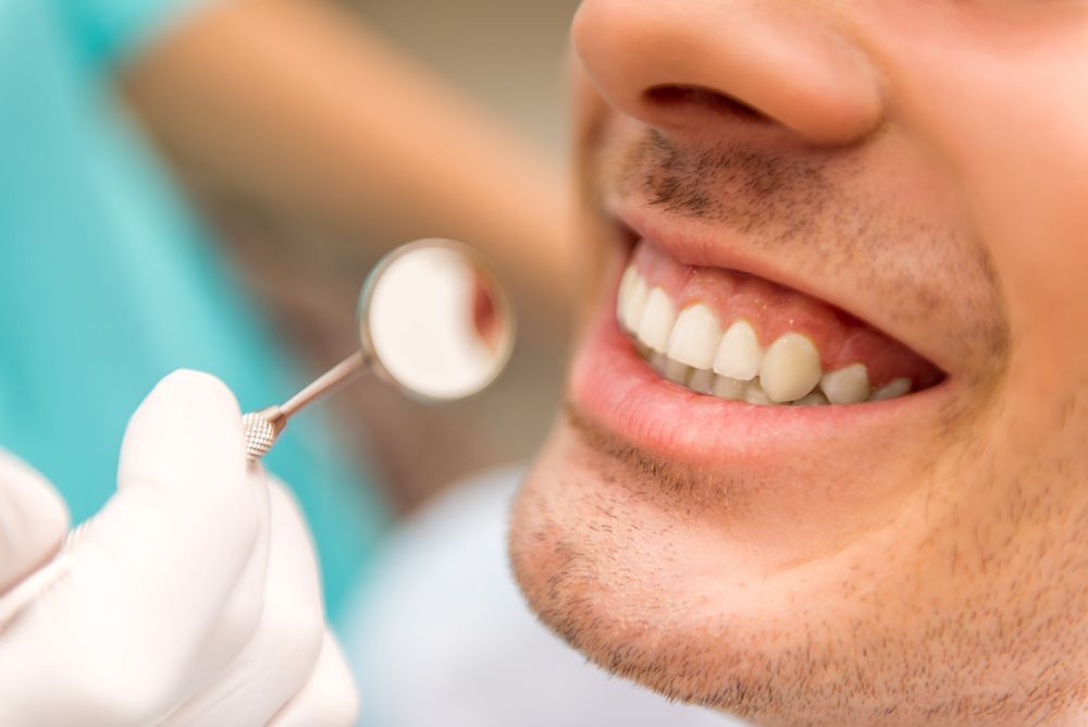 A dental mirror and a close up of a man's smile